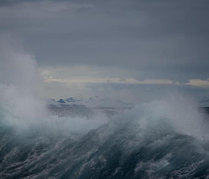 the ocean appears to be tumultuous with waves crashing against the shore. The sky is overcast with dark clouds